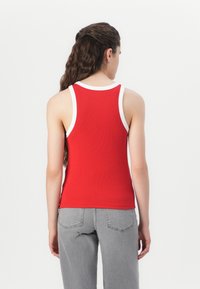 Rot gestreifter Tanktop mit weißem Saum, besitzt ein figurbetontes Design und ärmellosen Schnitt. Kombiniert mit grauen hochgeschnittenen Jeans.
