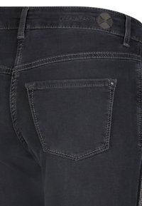 Jeans de mezclilla negros con un bolsillo trasero con una ligera curva, costuras visibles y una etiqueta de logo encima de la cinturilla. Textura suave.