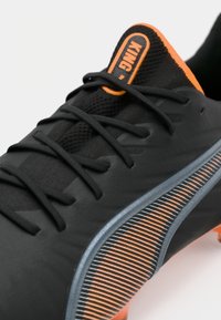 Scarpe da calcio nere con accenti arancioni, mesh testurizzato e un design a strisce lungo il lato. I lacci neri e la linguetta con marchio completano il look.
