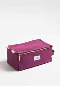 Lila canvasväska med en gyllene dragkedja och ett brunt läderhandtag. Har repdetaljer och en vit logotag på ena sidan. Rektangulär form.