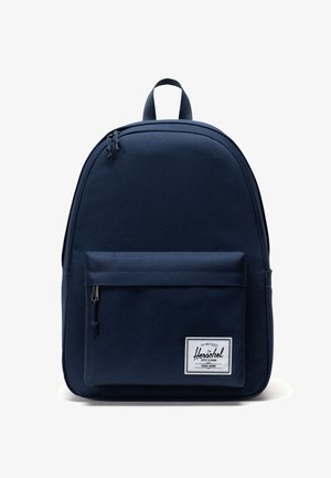 Navy blue backpack with a smooth fabric texture, rounded shape, front pocket with zipper, and a white logo label. Adjustable straps.