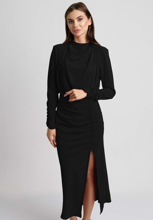 Czarna, długa sukienka z długimi rękawami, z marszczeniem po boku i rozcięciem do uda. Wykonana z gładkiego materiału, ma dopasowaną sylwetkę i subtelne drapowania.