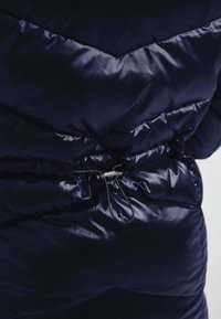 Marineblå dunjakke med en glossy finish, der har chevron-syninger, en indsnævret talje med en sort snor og toggle hardware detaljer.