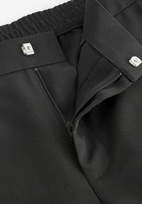 Pantalones de tela negra con una cremallera oculta, cierre de gancho de metal plateado y material texturizado. Acabado suave con cintura elástica.