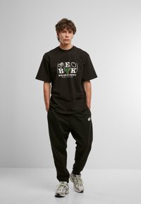 Sort kortærmet t-shirt med grafisk tryk, kombineret med sorte sweatpants. Har afslappet pasform og logo-detaljer. Casual fodtøj fuldender outfittet.