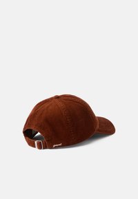 Căciulă din corduroy maro cu vizieră curbată, curea ajustabilă și logo brodat pe spate. Prezintă un design de țesătură texturată, cu benzi.