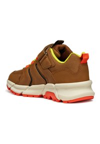Chaussure de sport marron avec une tige texturée, des accents jaune fluo, une sangle ajustable et une semelle en caoutchouc multicolore avec des surlignements rouges.