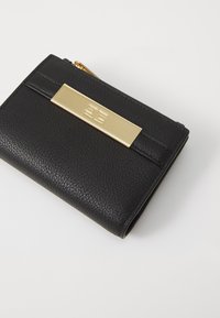 Black textured leather wallet with a gold-tone rectangular hardware accent and zipper closure, featuring a minimalistic design and subtle branding.