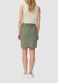 Jupe en denim vert olive avec un design ajusté, longueur mi-cuisse, deux poches arrière et une texture lisse. Des baskets blanches sont portées.