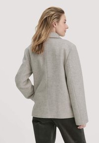 Graue Jacke aus Wollmischgewebe mit strukturiertem Design, Reverskragen und langen Ärmeln. Glatte Textur, figurbetonte Silhouette und minimale Nähte.