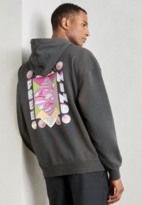Grijze hoodie met een groot, kleurrijk grafisch ontwerp op de achterkant met de tekst "FREE MINDS" en abstracte patronen, gemaakt van een zachte stof.