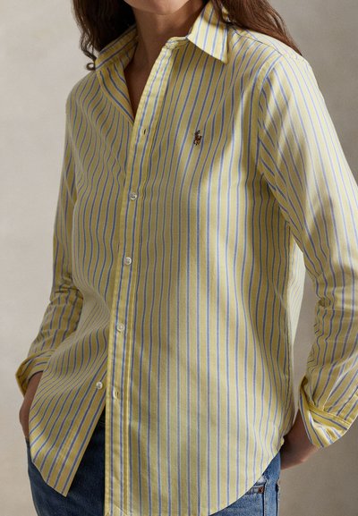 Πουκάμισο με κουμπιά σε ανοιχτό κίτρινο χρώμα με μπλε ρίγες, διαθέτει γιακά, μακριά μανίκια και μικρό κεντημένο λογότυπο στο στήθος.