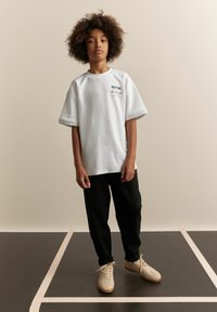 Overdimensioneret hvid bomulds t-shirt med sort "NEW YORK" print, parret med sorte sweatpants og beige sneakers med en struktureret overflade.