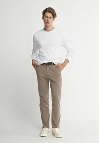 Weißes Langarmhemd, beige Hose, brauer Gürtel und helle Schuhe. Einfaches Design mit lockerer Passform, ohne sichtbare Muster oder Logos.