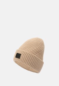 Gorro de punto color beige con textura acanalada, puño doblado y un pequeño detalle de etiqueta de cuero negro en el lateral.