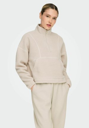 Beige fleece pullover with half-zip, slightly cropped length, ribbed cuffs, and a kangaroo pocket. Soft texture and relaxed fit.
