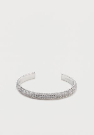 Bracciale a polsino in argento con una superficie liscia e lucidata e una fila di piccole pietre chiare lungo il bordo superiore. Materiale metallico resistente.