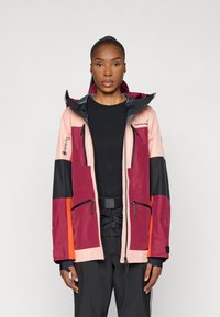 Χρωματιστό μπουφάν με υλικό GORE-TEX. Διαθέτει ροζ, σκούρο κόκκινο, μαύρες και πορτοκαλί περιοχές. Συμπεριλαμβάνει δύο μπροστινές τσέπες με φερμουάρ και ρυθμιζόμενη κουκούλα.