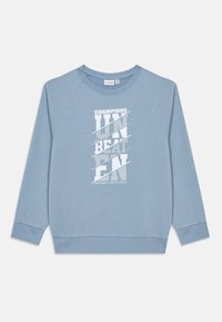 Sweatshirt bleu clair en tissu doux, avec un design graphique en texte blanc comportant "CHAMPIONS" et "UNBEATEN" en police grasse.