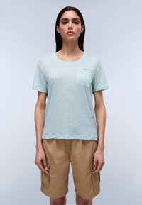 Błędny niebieski, krótki rękaw t-shirt wykonany z teksturowanej tkaniny z kieszenią na piersi. Połączony z beżowymi szortami cargo z bocznymi kieszeniami.