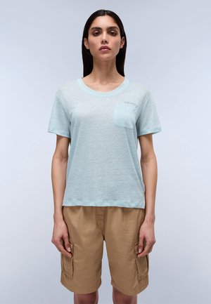 Helles blaues T-Shirt mit kurzen Ärmeln aus strukturiertem Stoff und einer Brusttasche. Kombiniert mit beigefarbenen Cargo-Shorts mit Seitentaschen.