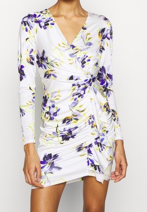 Vestido floral blanco con mangas largas, que presenta patrones de flores moradas y amarillas, un diseño envolvente y detalles fruncidos en el costado.