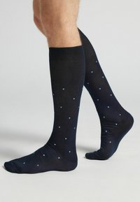 Calcetines de rodilla en color marino con un patrón geométrico de pequeñas formas azul claro distribuidas uniformemente por la tela. Textura suave.