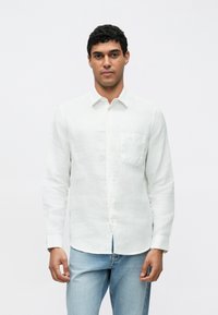 Camisa branca de linho de manga comprida com fecho de botões frontal, bolso único no peito e colarinho clássico, combinada com jeans de ganga azul claro.