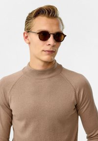 Beige coltrui met een zachte textuur en raglanmouwen, gecombineerd met ronde zonnebril met bruine glazen en schildpadaccenten.