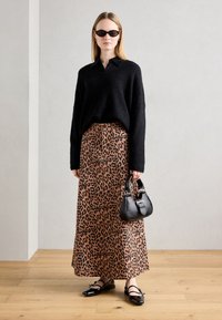 Musthave musta pehme kudum, leopardimustriga maxi-seelik oranži ja pruuni tooniga, must käsitasku ja mustad jalanõud kinnitusdetailiga. Kandmiseks ovaalsed prillid.