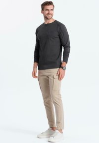 Tummanharmaa pitkähihaisessa paidassa on tasku, ja se on yhdistetty vaaleanbeigeihin cargo-housuihin, joissa on sivutaskut. Mallilla on päällään valkoiset urheilukengät.