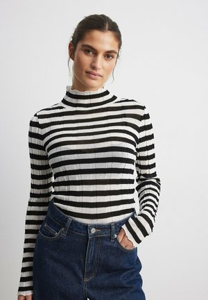 Black and white striped turtleneck sweater with long sleeves, ribbed texture, and a fitted design paired with high-waisted denim jeans.
