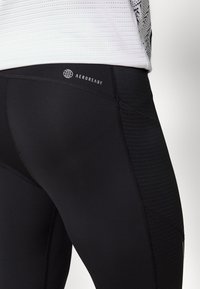 Black athletic leggings featuring a smooth texture, a snug fit, and AEROREADY branding on the waistband. Subtle patterned accents along the side.
