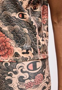 Gros plan sur un vêtement de sport avec des motifs floraux et ondulés noirs et roses, montrant des coutures cousues et un petit logo Champion.