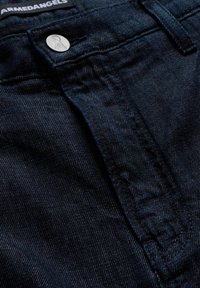 Tessuto di denim scuro con una texture sottile, caratterizzato da un bottone argentato e cuciture a contrasto. Il design include uno stile classico a cinque tasche.
