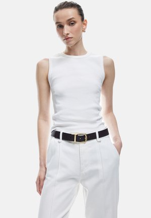 Witte geribde tanktop met schouderuitsnijdingen, gecombineerd met witte hoge taille plooibroek. Accentueert met een zwarte riem met een gouden gesp.