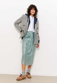 Blazer croisé à rayures grises au-dessus d'un hoodie bleu, d'une chemise blanche et d'une jupe en sequins turquoise. Chaussures marron avec des chaussettes grises.