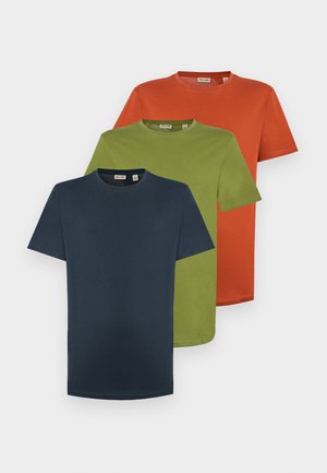 Granatowy, krótki rękaw t-shirt w połączeniu z jasnoszarymi, prostymi dżinsami oraz beżowymi tenisówkami, na tle jednolitego białego tła.