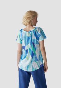 Short-sleeve top featuring a blue and green abstract floral pattern on a light background, with a gathered neckline and relaxed fit.