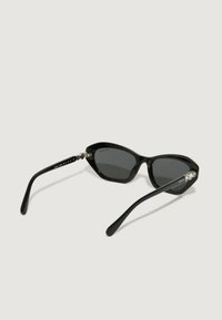 Mustad musta cat-eye päikeseprillid läikiva viimistlusega. Omavad halli klaasi, elegante käeosi ja kaunistust hõlpsustusosas.