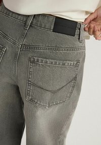 Szare dżinsy w średnim stanem, z czarną metką z napisem "Diverse Jeans" oraz dwiema tylnymi kieszeniami z teksturowanym przeszyciem.