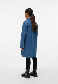 Vidutinio mėlynumo džinsinė suknelė, ilgomis rankovėmis, laisvo kirpimo, iki kelių, su užsegamu priekiu ir dviem šoniniais kišenėmis, derinama su juodais kareiviškais batais.