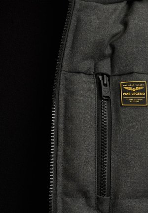 Zwarte zip-up jas van een gemêleerde stof. Heeft een zak met een zwarte rits en een rechthoekig label met de "PME LEGEND" branding.