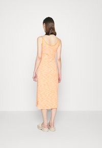 Vestido midi laranja com um padrão ondulado, alças finas e design de costas abertas. Combinado com sandálias de plataforma bege. Textura suave.