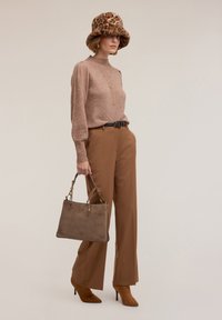 Brązowy prążkowany sweter, beżowe spodnie z wysokim stanem, brązowe zamszowe szpilki, futrzana czapka w panterkę i szara torba na ramię ze złotymi akcentami.