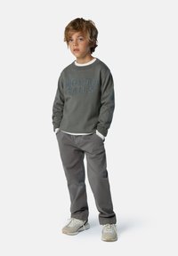 Grauer Sweatshirt mit blauer "NORTH SAILS" Aufschrift, über einem weißen Langarmshirt getragen. Graue Hose und beige Sneaker runden den Look ab.