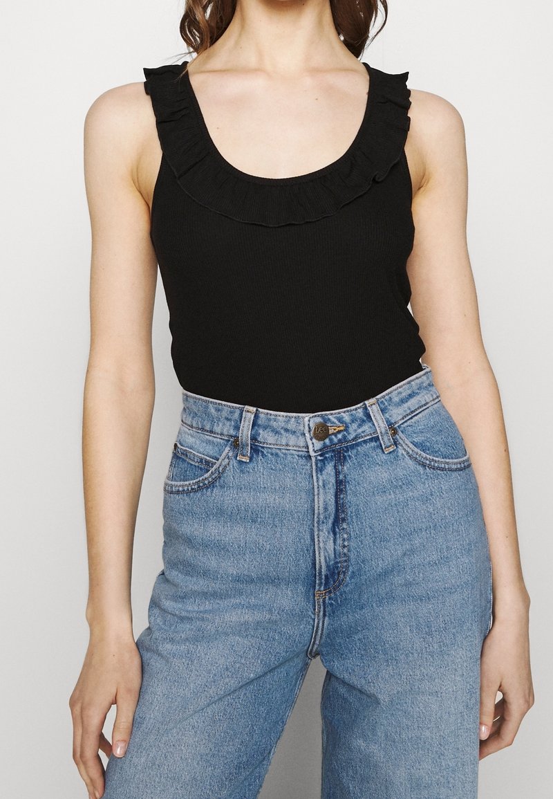 Svart ribbad linne med volangkant, kombinerat med högmidjade ljust blå denimjeans med knappstängning och sidofickor.