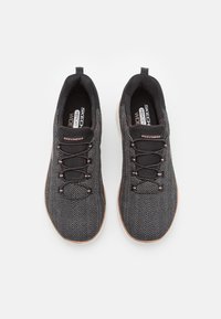 Chaussures de sport noires avec un motif en chevrons, dotées de lacets, de rembourrage en mousse à mémoire de forme et d'une semelle texturée en couleur contrastante.