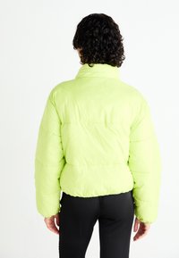 Light green puffer jacket with long sleeves, high collar, and elastic hem. Material appears smooth with vertical quilted sections.