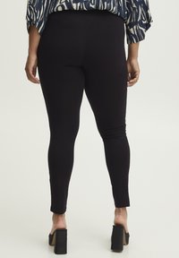 Leggings neri con una texture liscia, design aderente e taglio alla caviglia. Abbinati a sandali neri con tacco alto e spesso.
